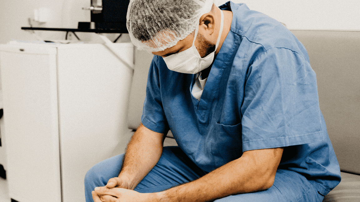 A picture of a male surgeon sat on a sofa holding his hands together
